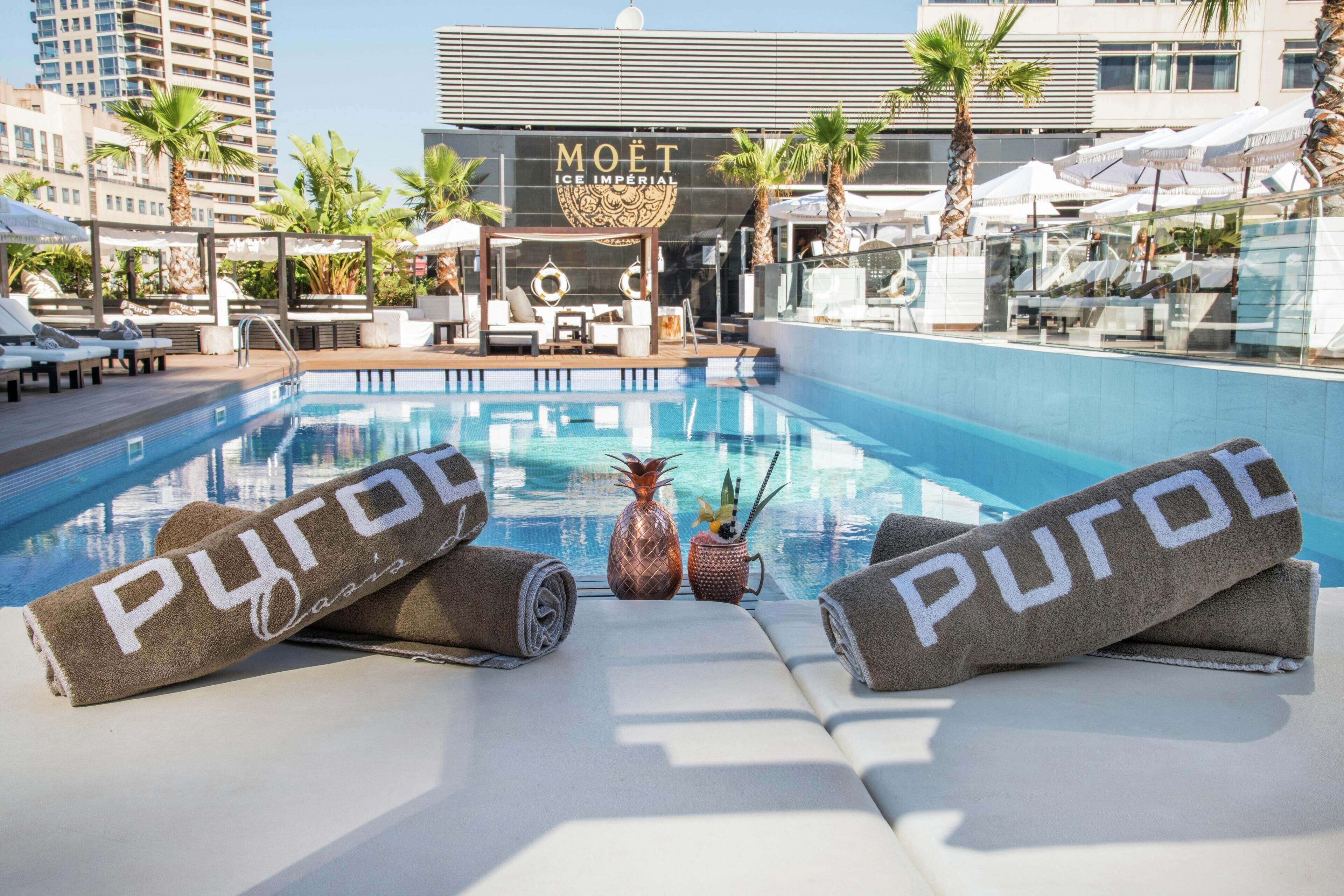 Un área junto a la piscina con sillas de descanso, toallas y un cartel de Moët Ice Imperial al fondo.
