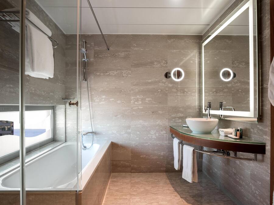 Un baño moderno con ducha de mampara de vidrio, una bañera amplia y un tocador con encimera de cristal.