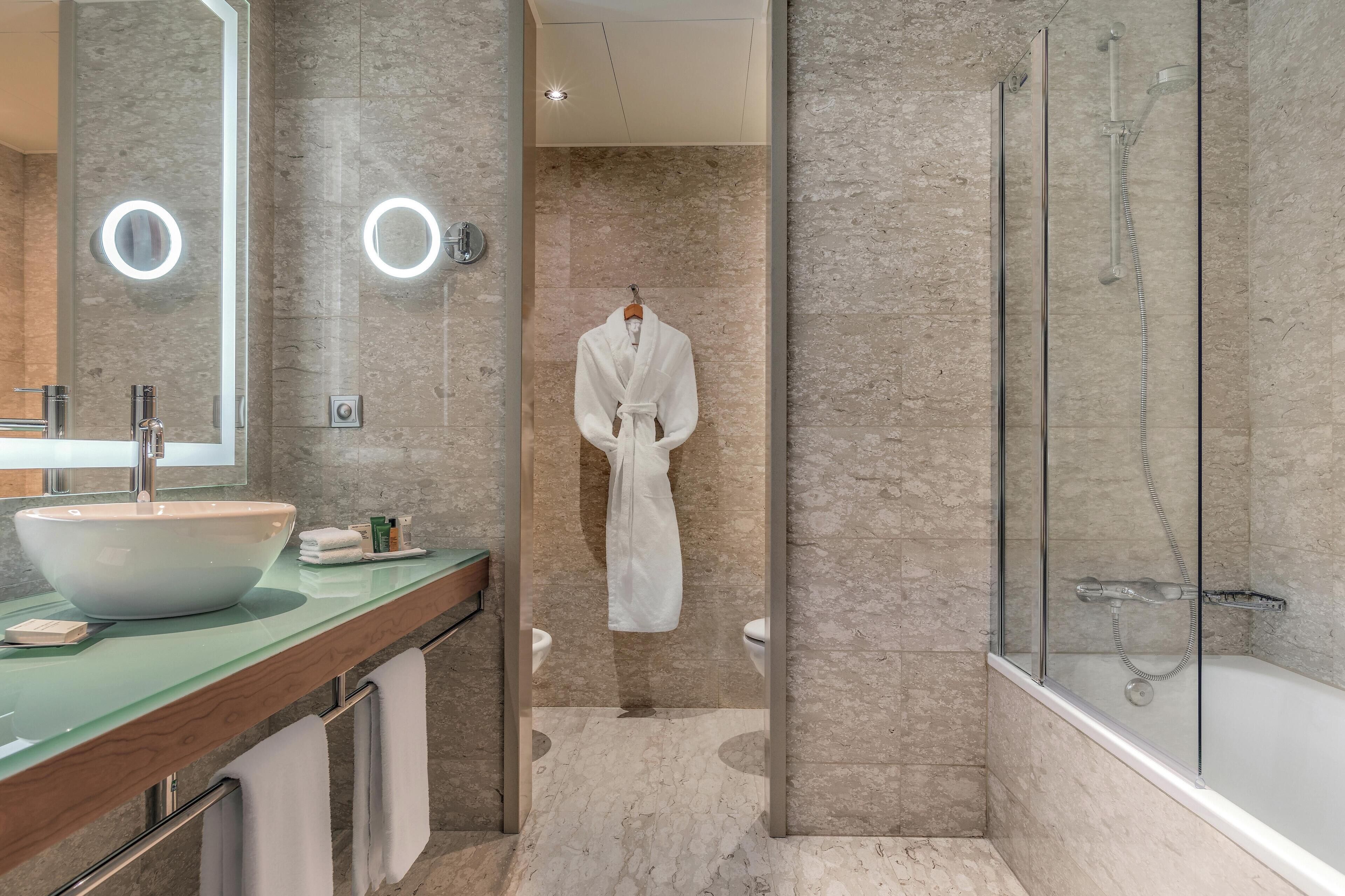 A modern bathroom with a large mirror, a white sink, a glass-enclosed shower, and a robe hanging on a rack.