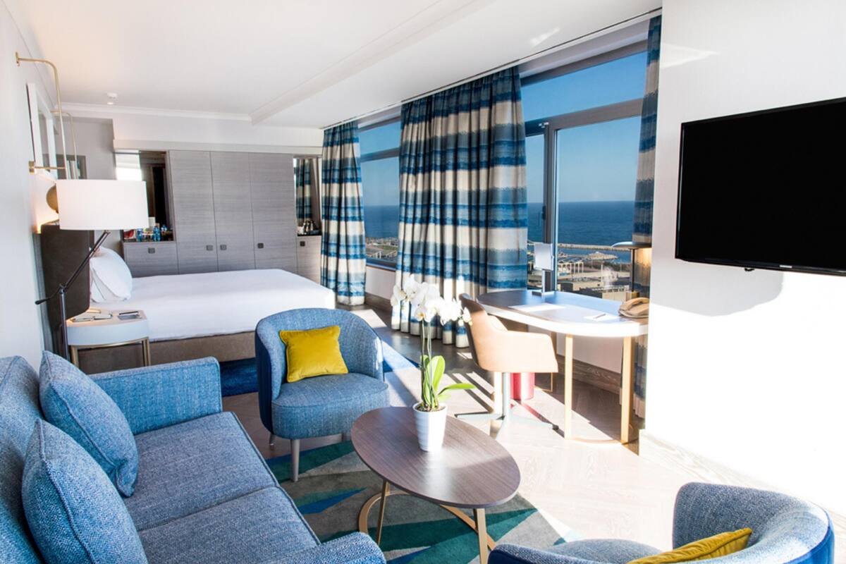 A modern hotel room with a large bed, two sofas, a desk, and a TV.