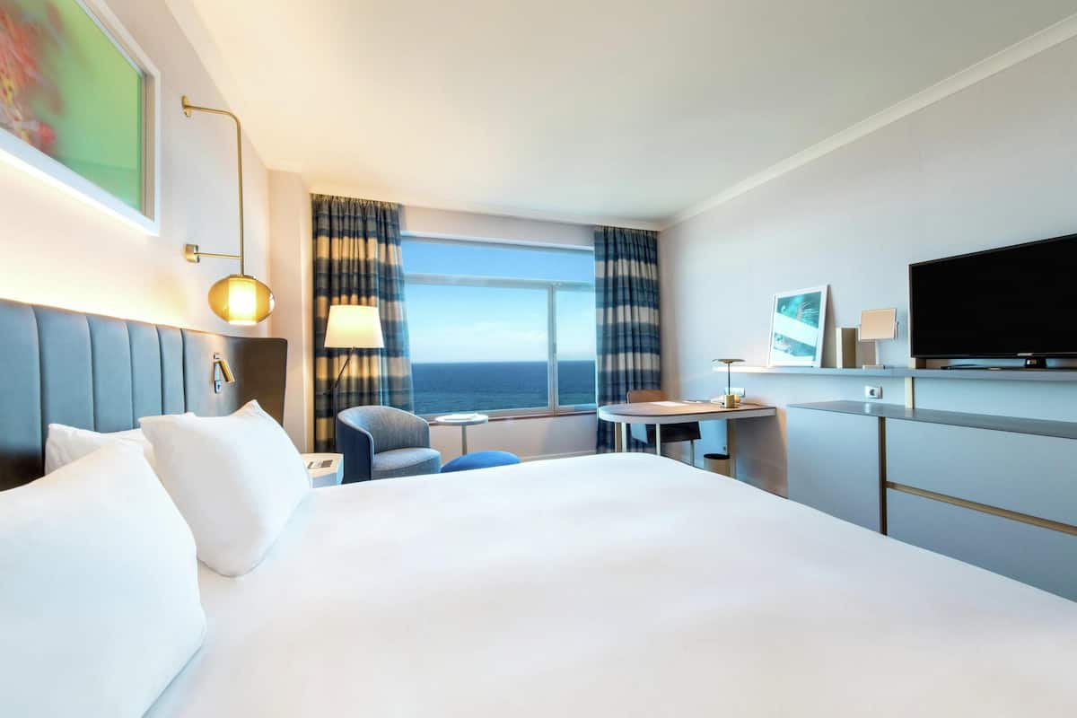 A hotel room with a large bed, a desk, a chair, a TV, and a window with curtains.