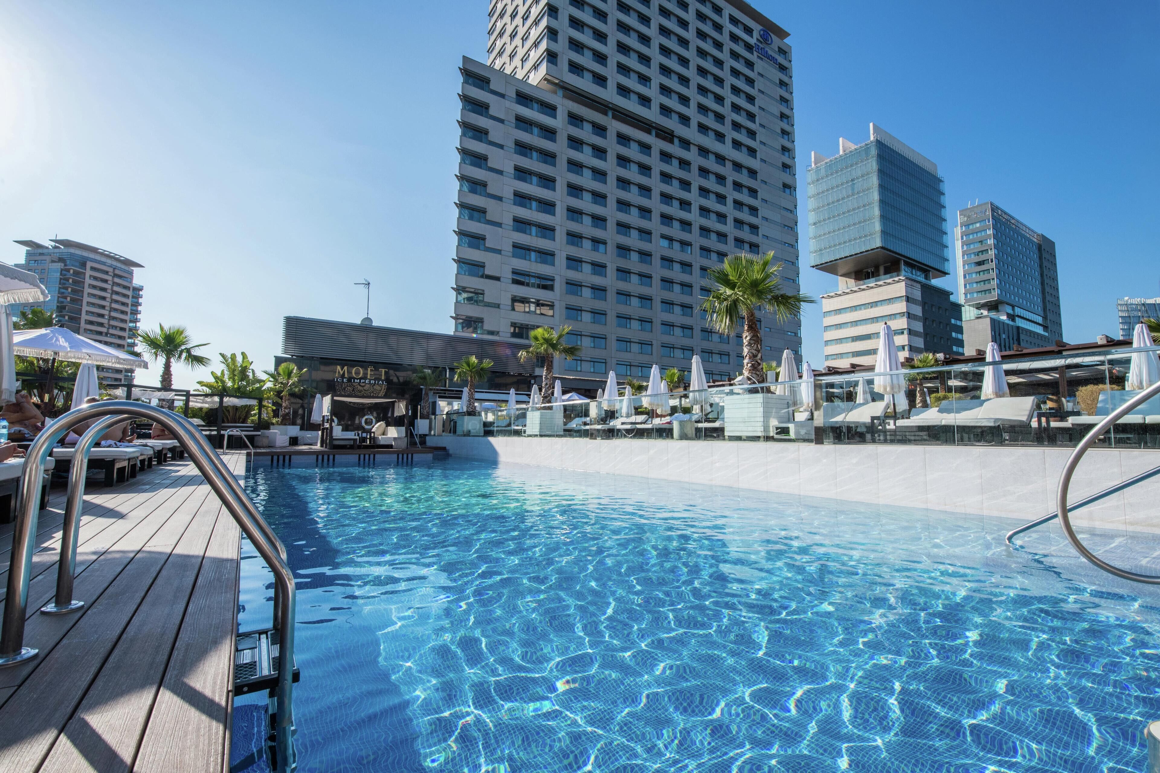 A swimming pool with a wooden deck, lounge chairs, and umbrellas.