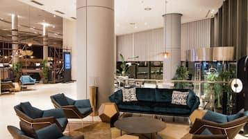 A modern lobby with a central seating area, a bar, and a large window overlooking the interior.
