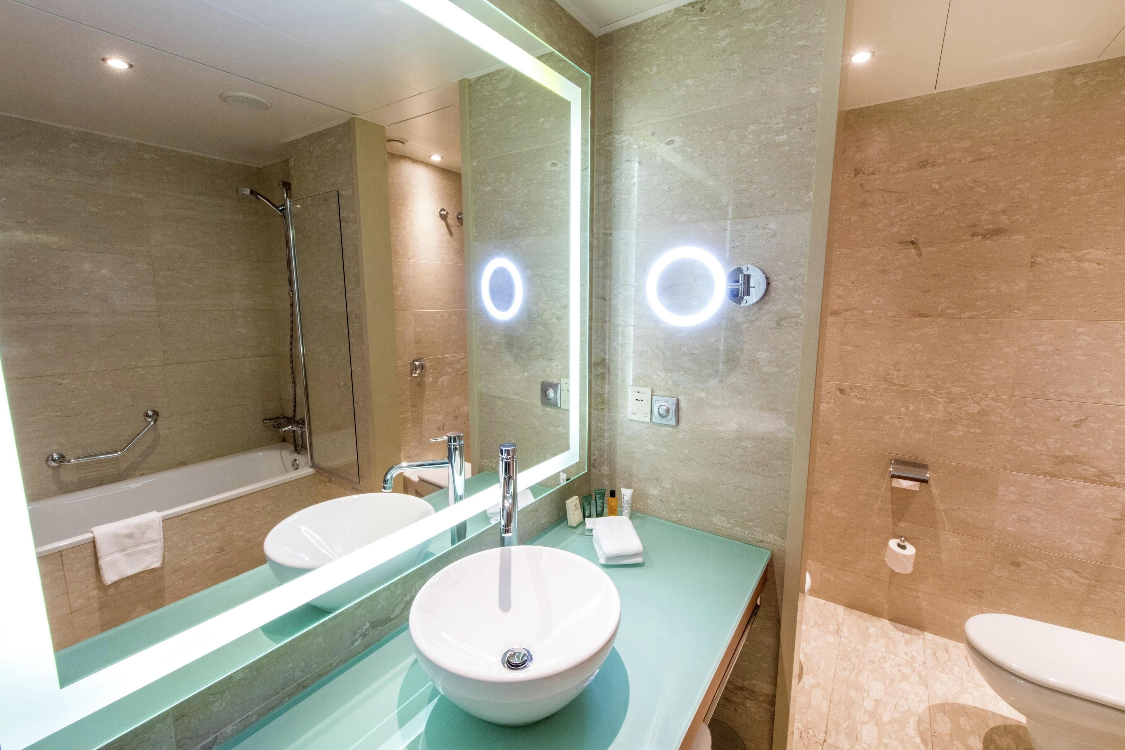 A modern bathroom with a large mirror, a sink, a bathtub, and a toilet.