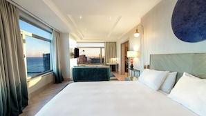 A hotel room with a large bed, a view of the city, a desk, and a chair.