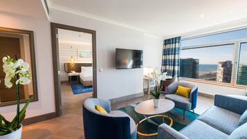 Ein modernes Hotelzimmer mit großem Fenster, einem Flachbildfernseher und einer Sitzecke mit blau-grauen Möbeln.