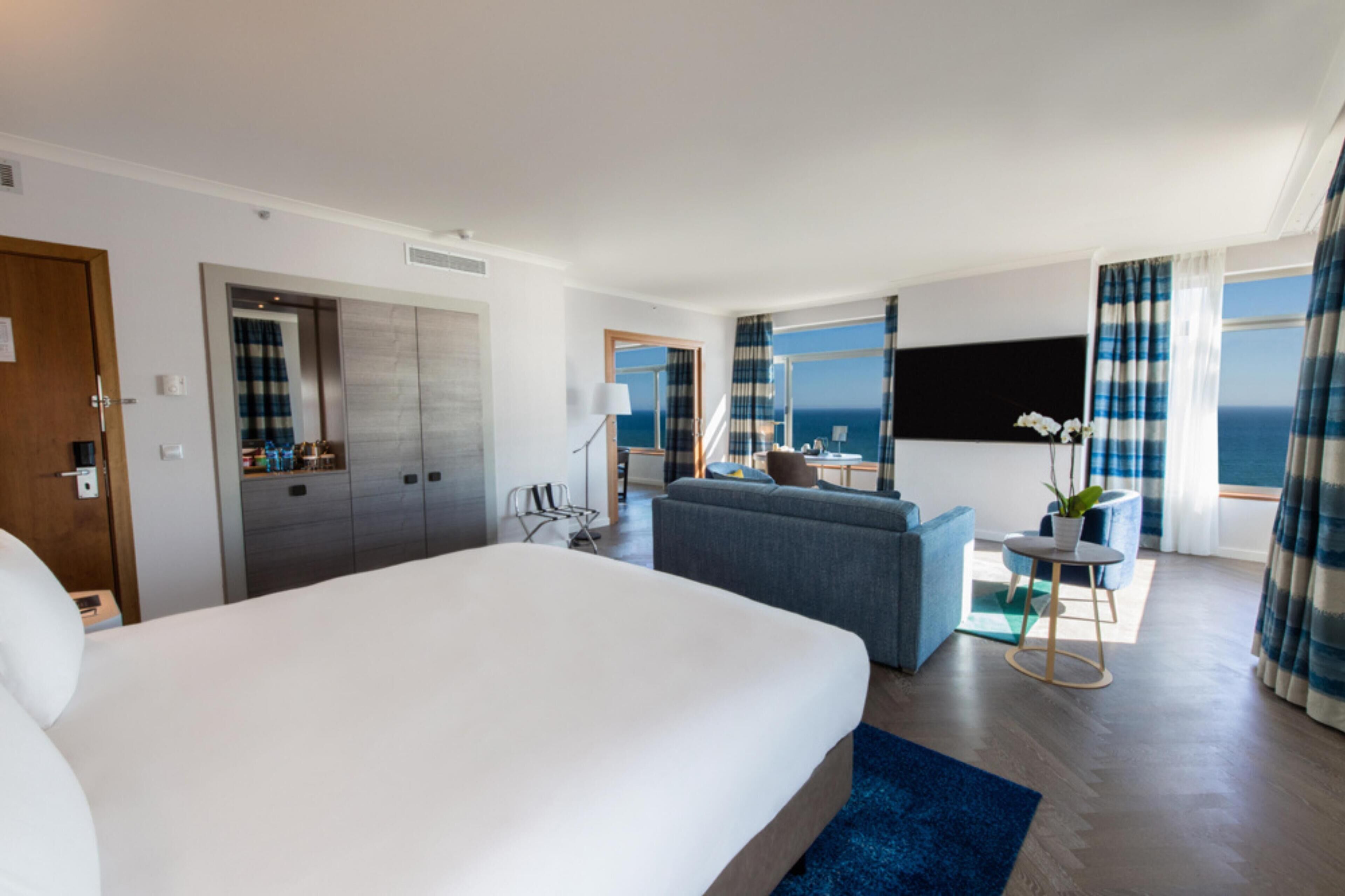 Een hotelkamer met een groot bed, een bank, een tafeltje en uitzicht op de oceaan.