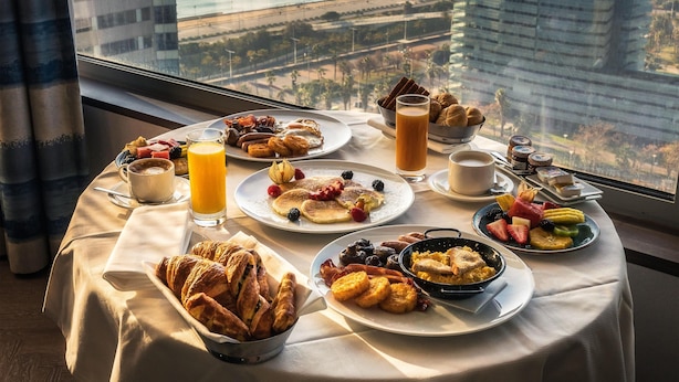 A breakfast table with various dishes, a glass of orange juice, and a view of the cityscape through a window.