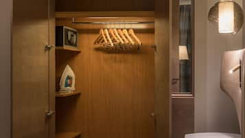 Un armario de madera con ropa colgada, un microondas y una repisa con una tetera.