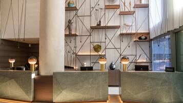 A modern hotel reception area with marble counters, geometric shelving, and pendant lighting.
