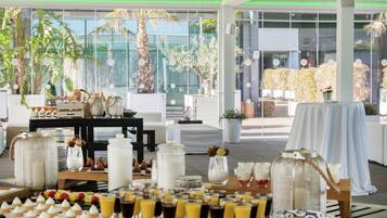 A breakfast buffet setup with various food items and drinks, surrounded by indoor plants and modern furniture.