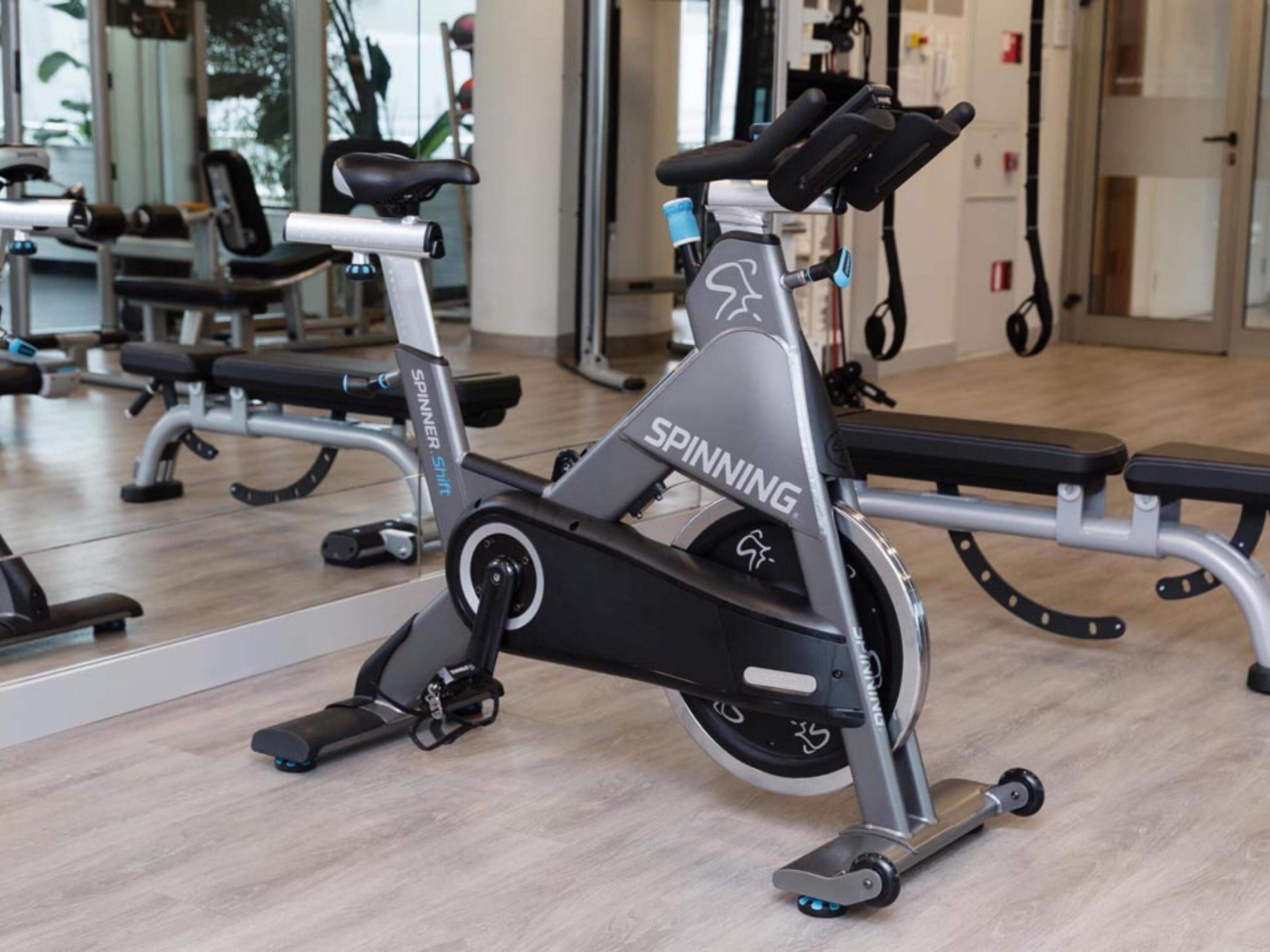 Un vélo d’appartement dans une salle de sport, avec un murmiroir et du matériel d’exercice en arrière-plan.