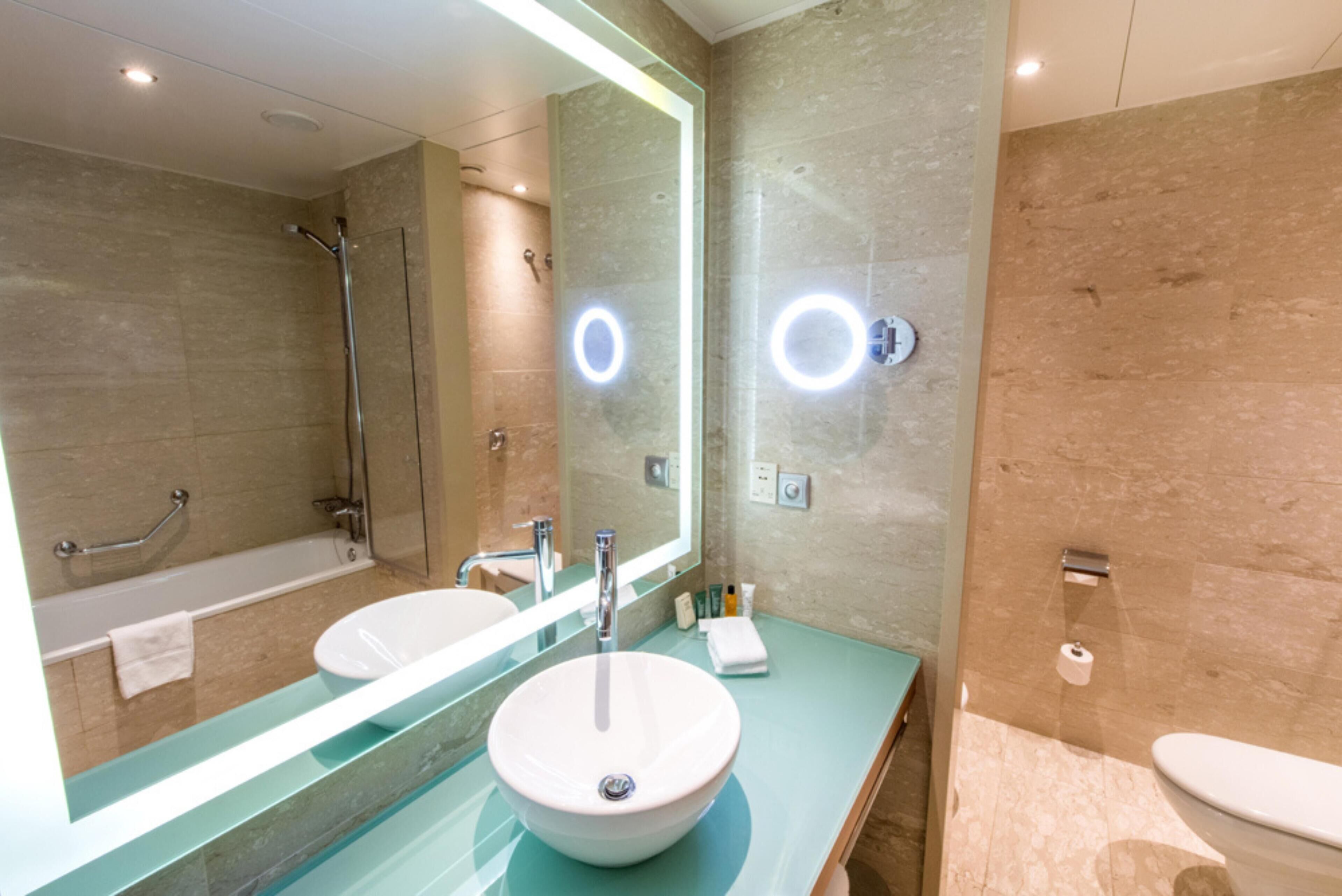 A modern bathroom with a large mirror, a sink, a bathtub, and a toilet.