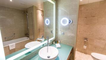 A modern bathroom with a large mirror, a sink, a bathtub, and a toilet.