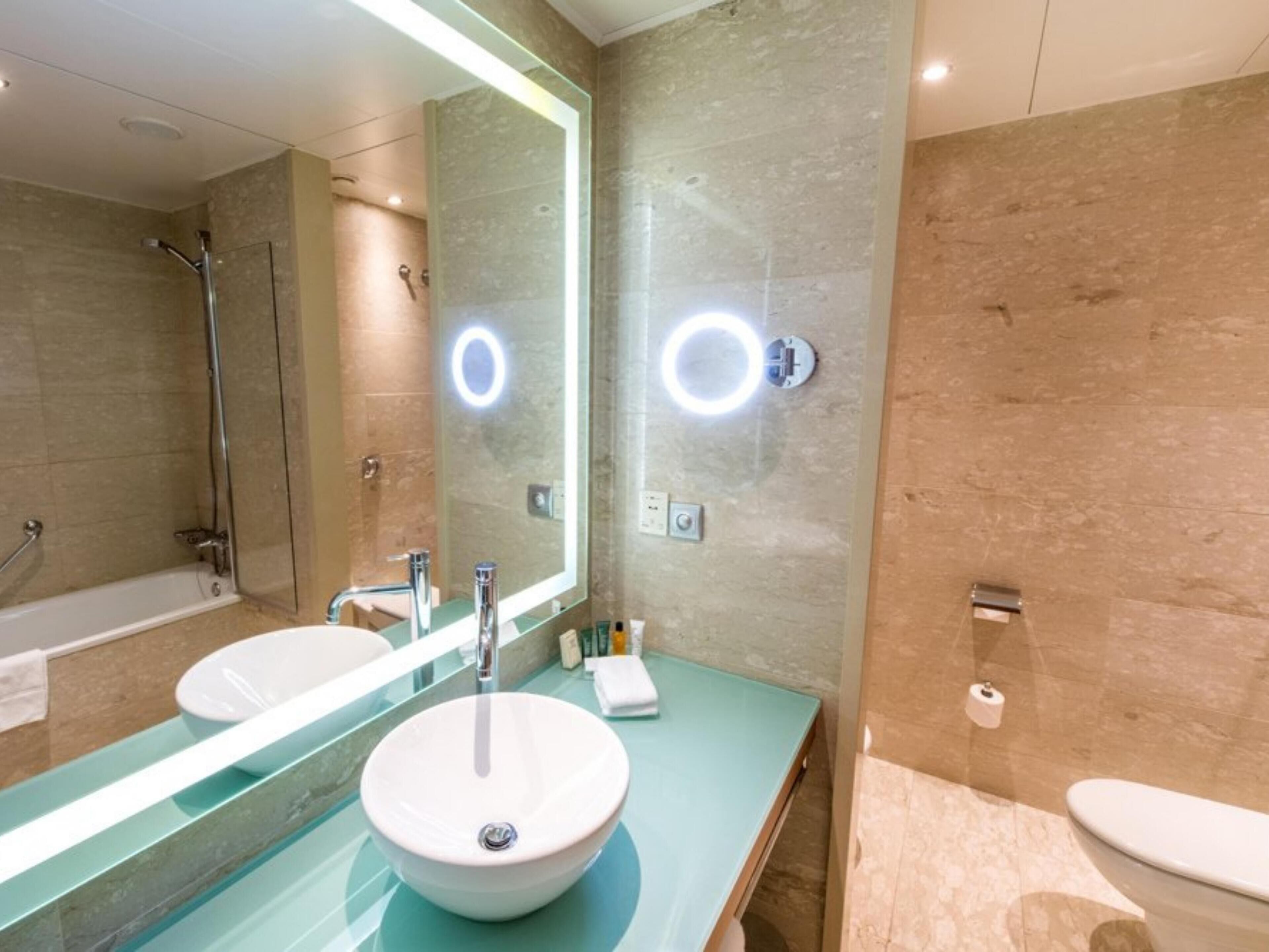 A modern bathroom with two sinks, a large mirror, and a bathtub.