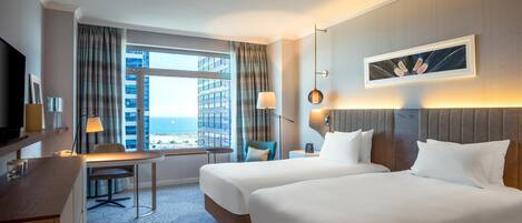 Une chambre d’hôtel avec deux lits, un bureau, une chaise, une télévision, une lampe et une vue sur la ville.