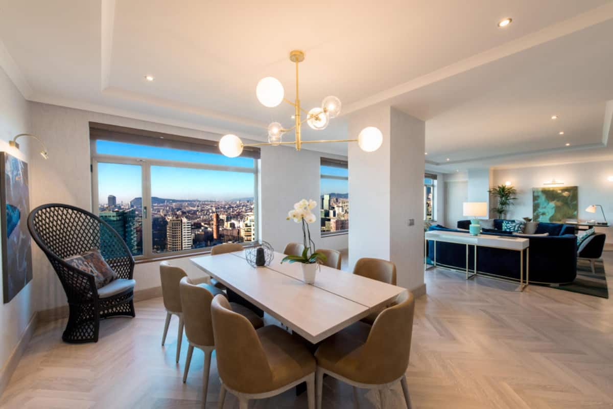 A modern dining area with a city view, a dining table, chairs, and a chandelier.