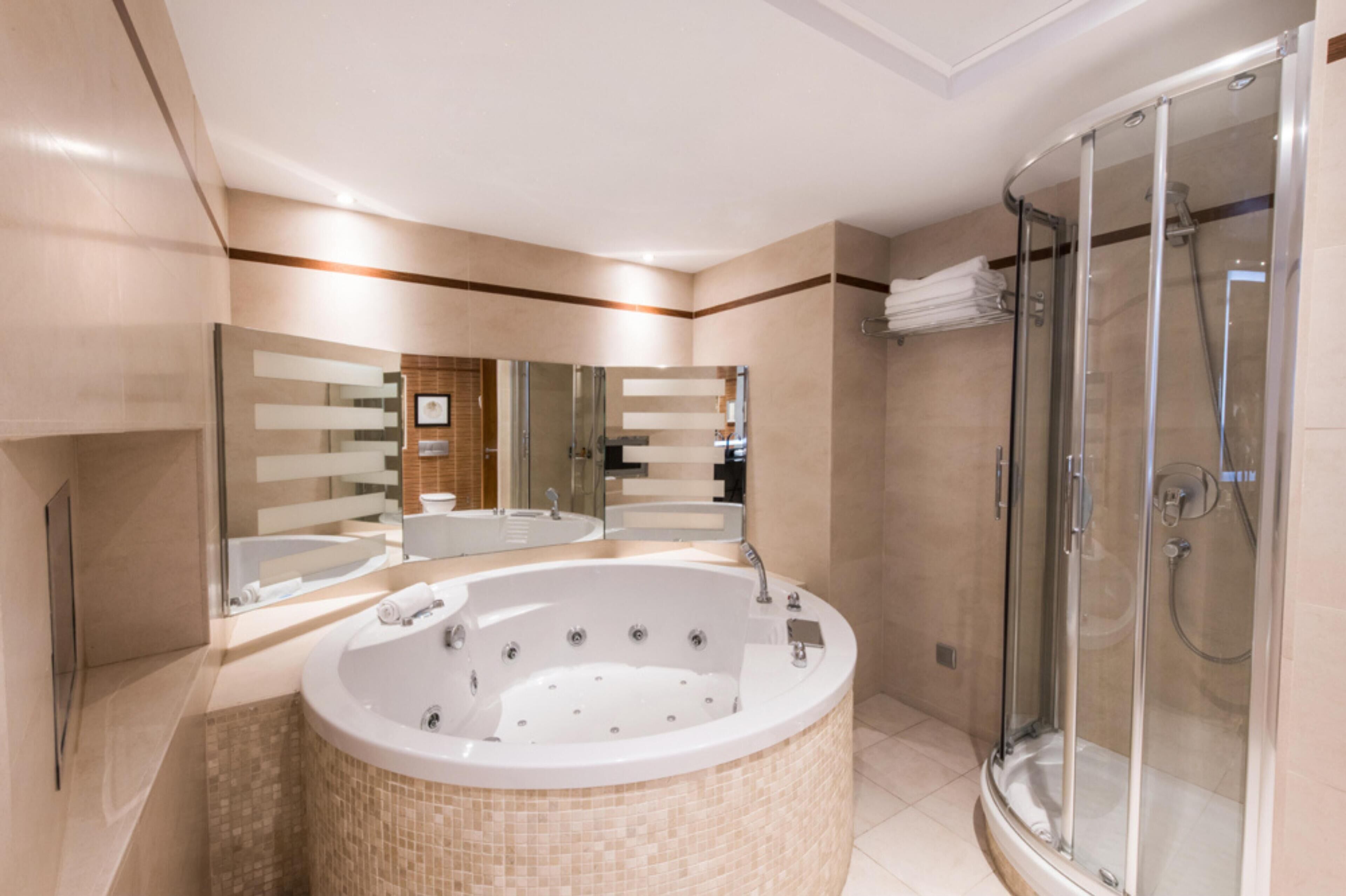Un baño moderno con una bañera grande, una ducha con cerramiento de vidrio y un espejo sobre el lavabo.