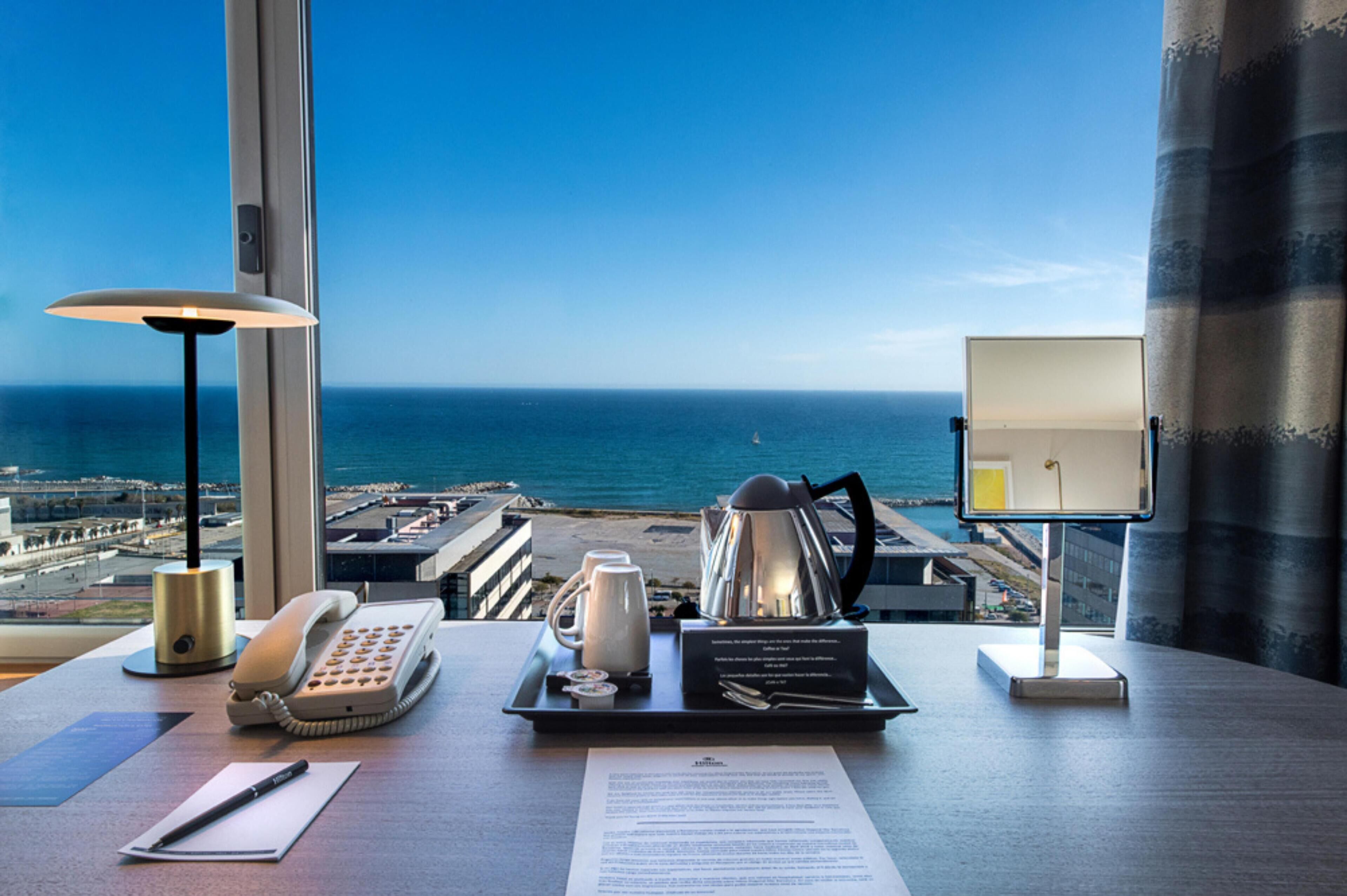 A hotel room with a desk, a telephone, a coffee pot, a tray with a cup and saucer, and a menu.