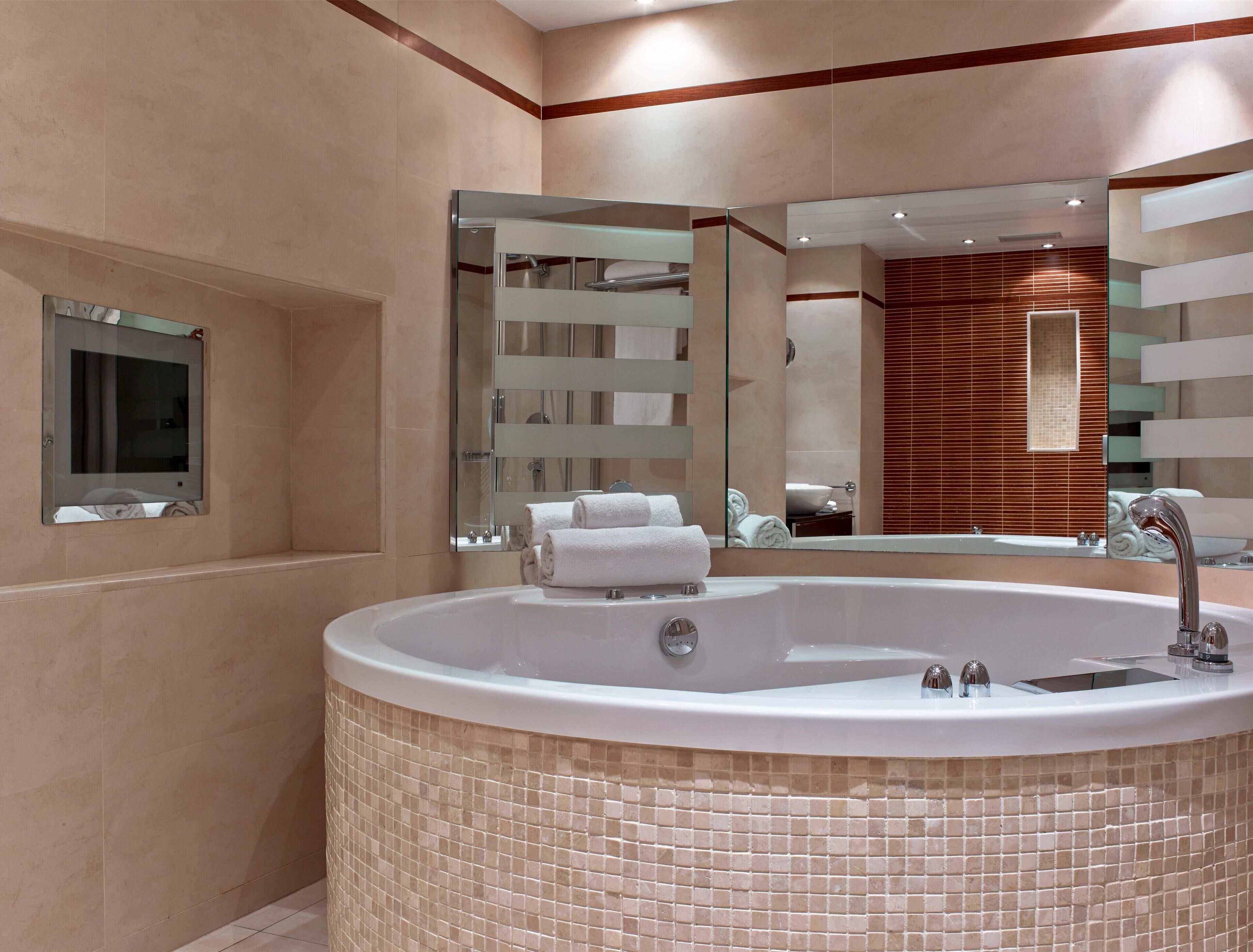 Un baño moderno con una bañera independiente grande, un espejo y un revestimiento de pared de madera.