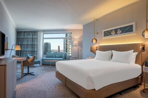 A modern hotel room with a large bed, a desk, a sofa, and a view of the cityscape. - Hilton Diagonal Mar Barcelona (Barcelona)