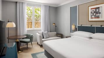 Una habitación de hotel con cama, sofá, escritorio y ventana con cortinas.