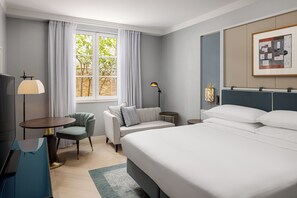 Una habitación de hotel con cama, sofá, escritorio y ventana con cortinas.