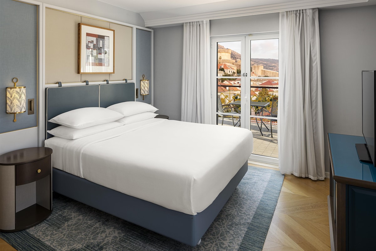 A hotel room with a large bed, a desk, and a view of the outdoors.