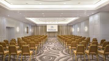 Ein Konferenzraum mit Reihen von Stühlen, dem Hilton-Logo und einem Teppichboden.