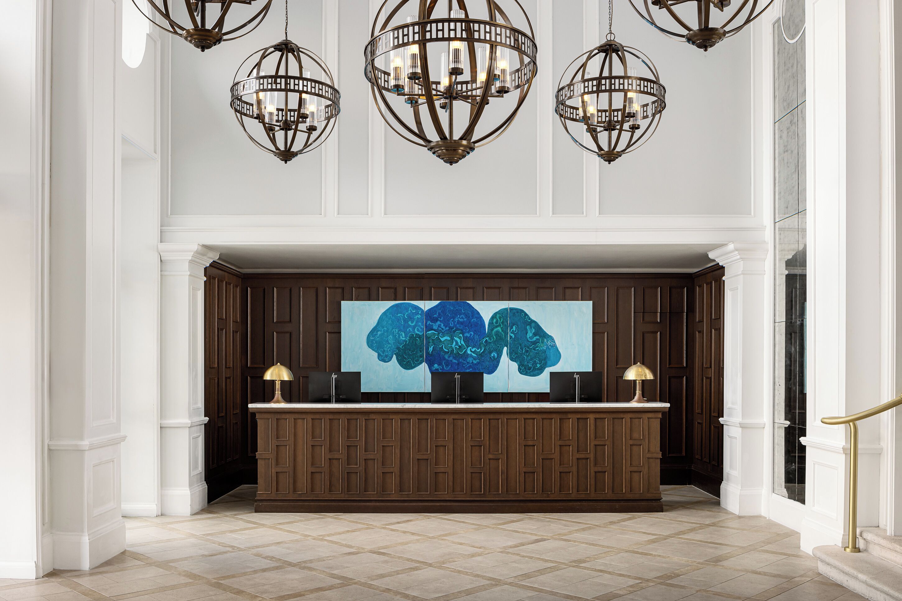 A reception area with a wooden reception desk, a large abstract painting, and three hanging chandeliers.