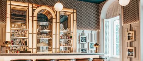 A bar area with shelves of bottles and glasses, a bar counter, and bar stools.