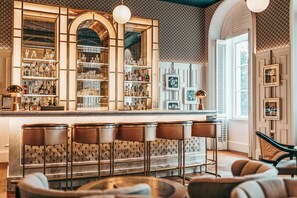 A bar area with shelves of bottles and glasses, a bar counter, and bar stools.