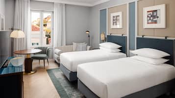 Une chambre d’hôtel avec deux lits, un bureau, une chaise, une lampe et une vue sur les bâtiments environnants.