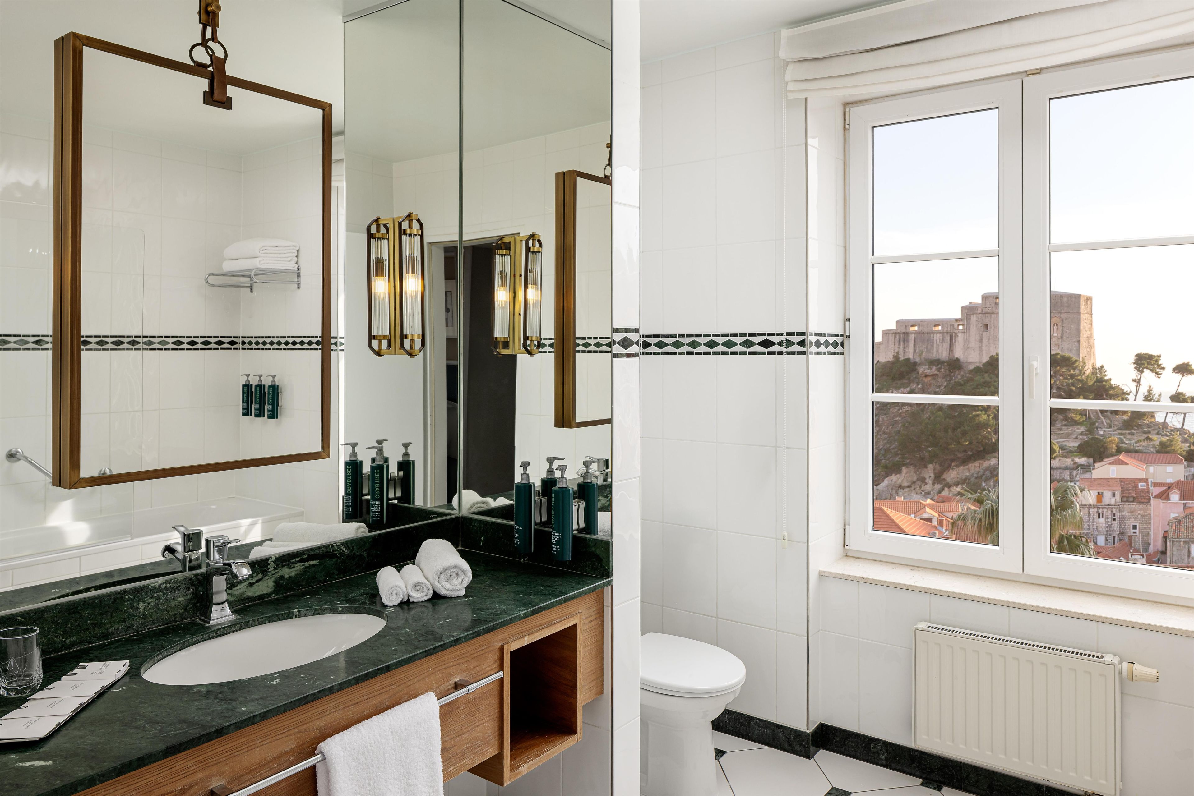 Un baño con un espejo grande, dos lavamanos, un inodoro y una ventana con vistas a edificios.