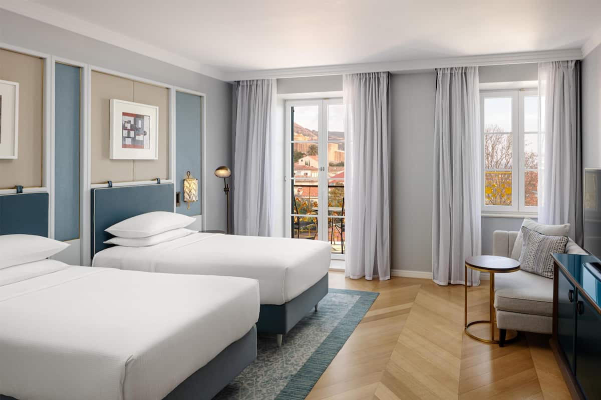A hotel room with two beds, a sofa, a TV, and a balcony with a view.