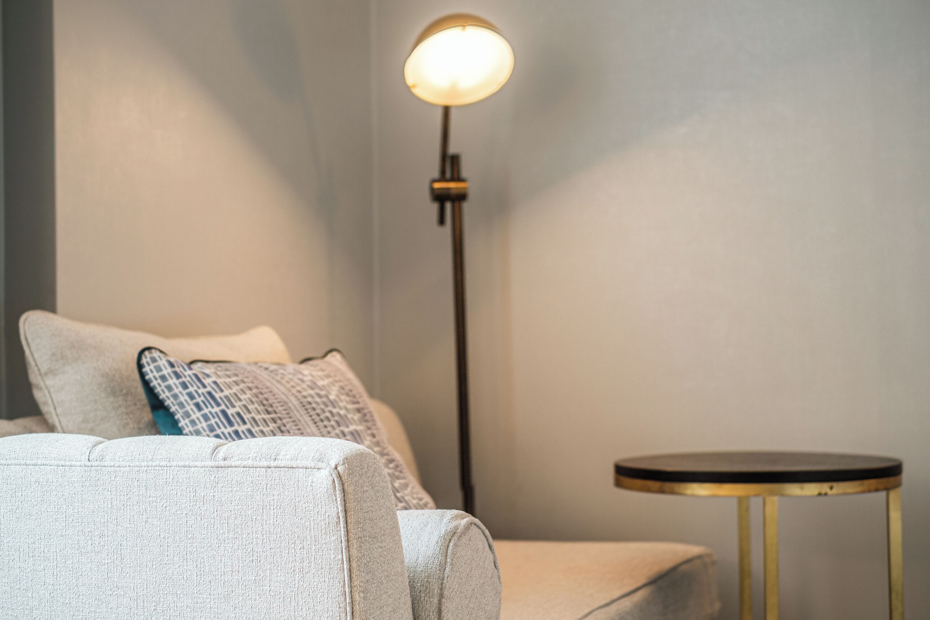 Une pièce avec un canapé, une petite table ronde et un lampadaire.