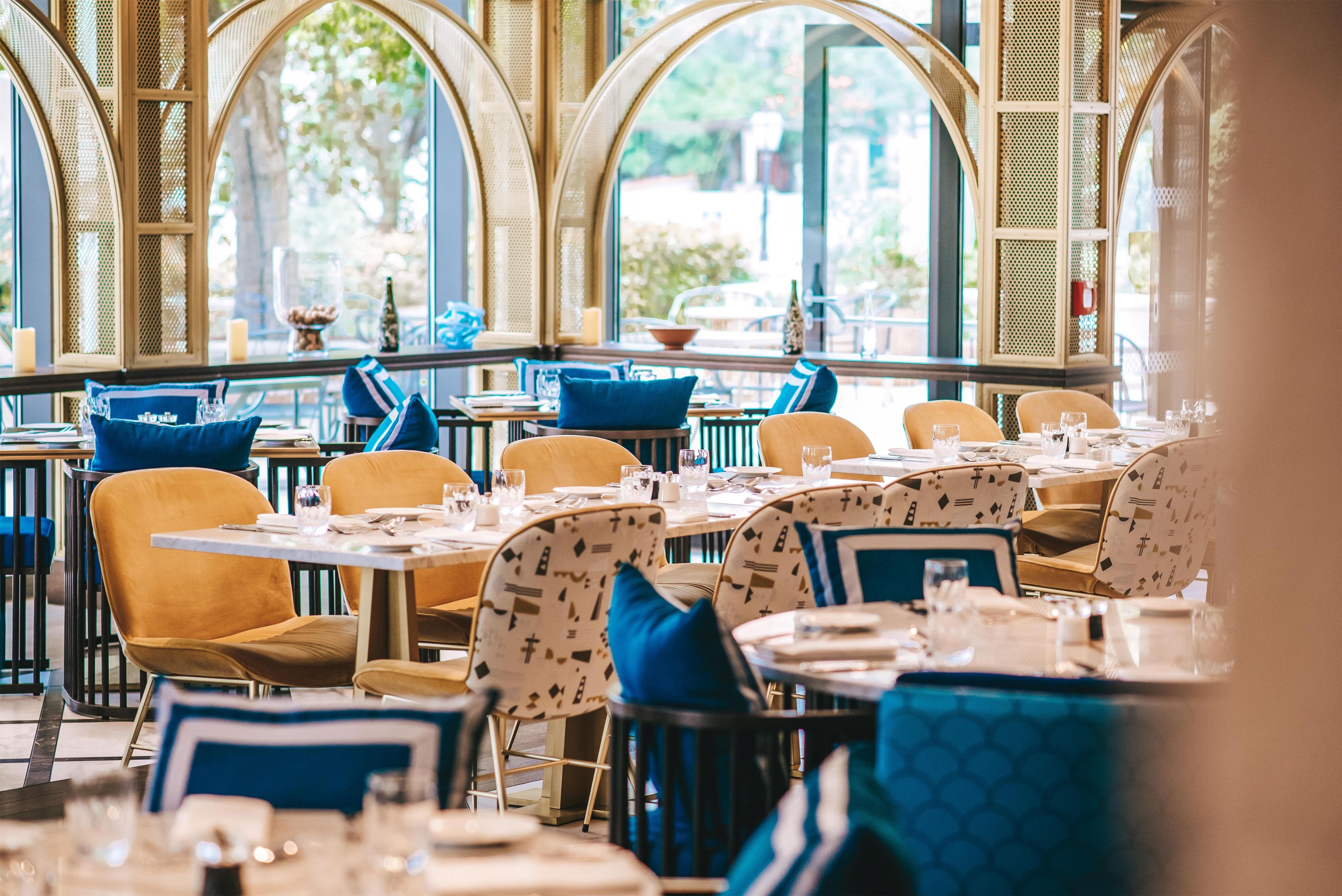 Um restaurante com mesas e cadeiras redondas, grandes janelas e vista para o exterior.