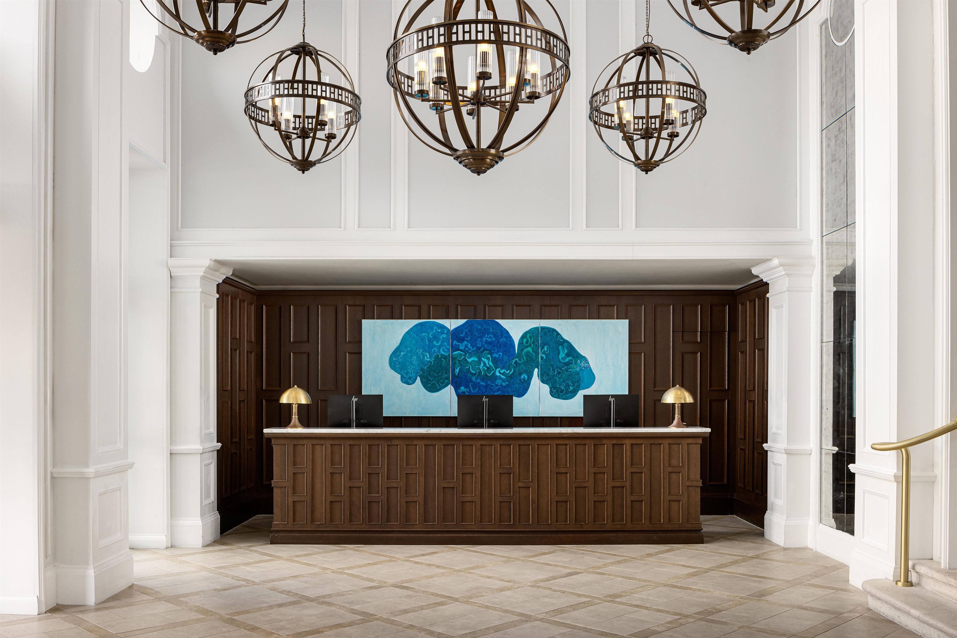 Zona de recepción con un panel de madera de fondo, un cuadro abstracto grande y un mostrador de recepción con dos lámparas.