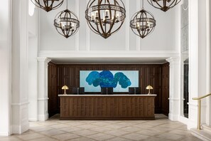 Zona de recepción con un panel de madera de fondo, un cuadro abstracto grande y un mostrador de recepción con dos lámparas.