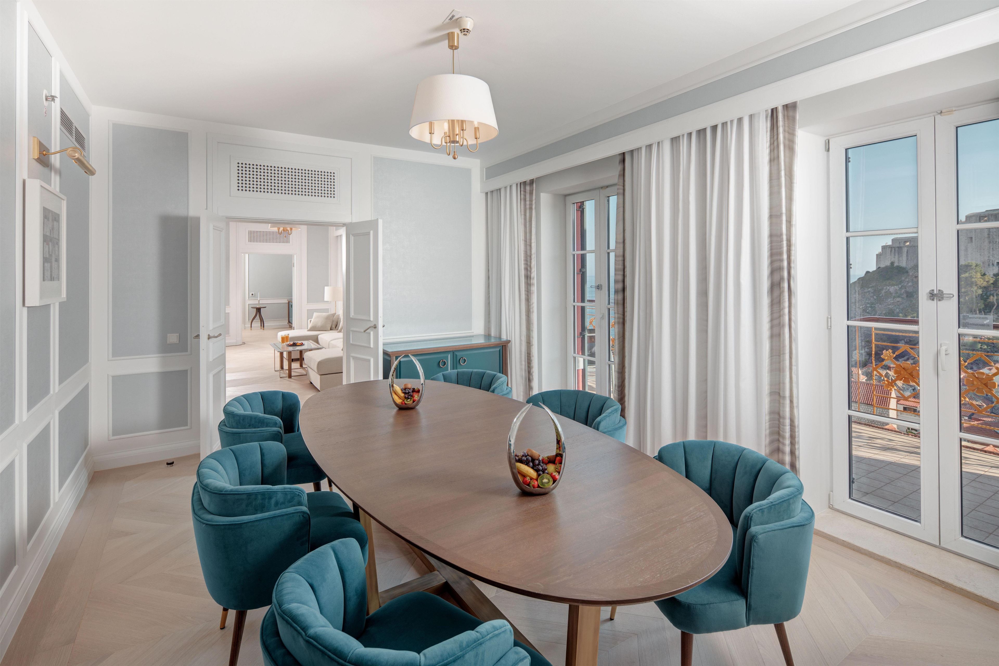 Comedor con una gran mesa ovalada, seis sillas color turquesa, un frutero y un candelabro moderno.