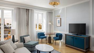 Un salon moderne comprenant un canapé, deux fauteuils, une table basse, un téléviseur posé sur un meuble et une vue dégagée grâce à de grandes fenêtres.