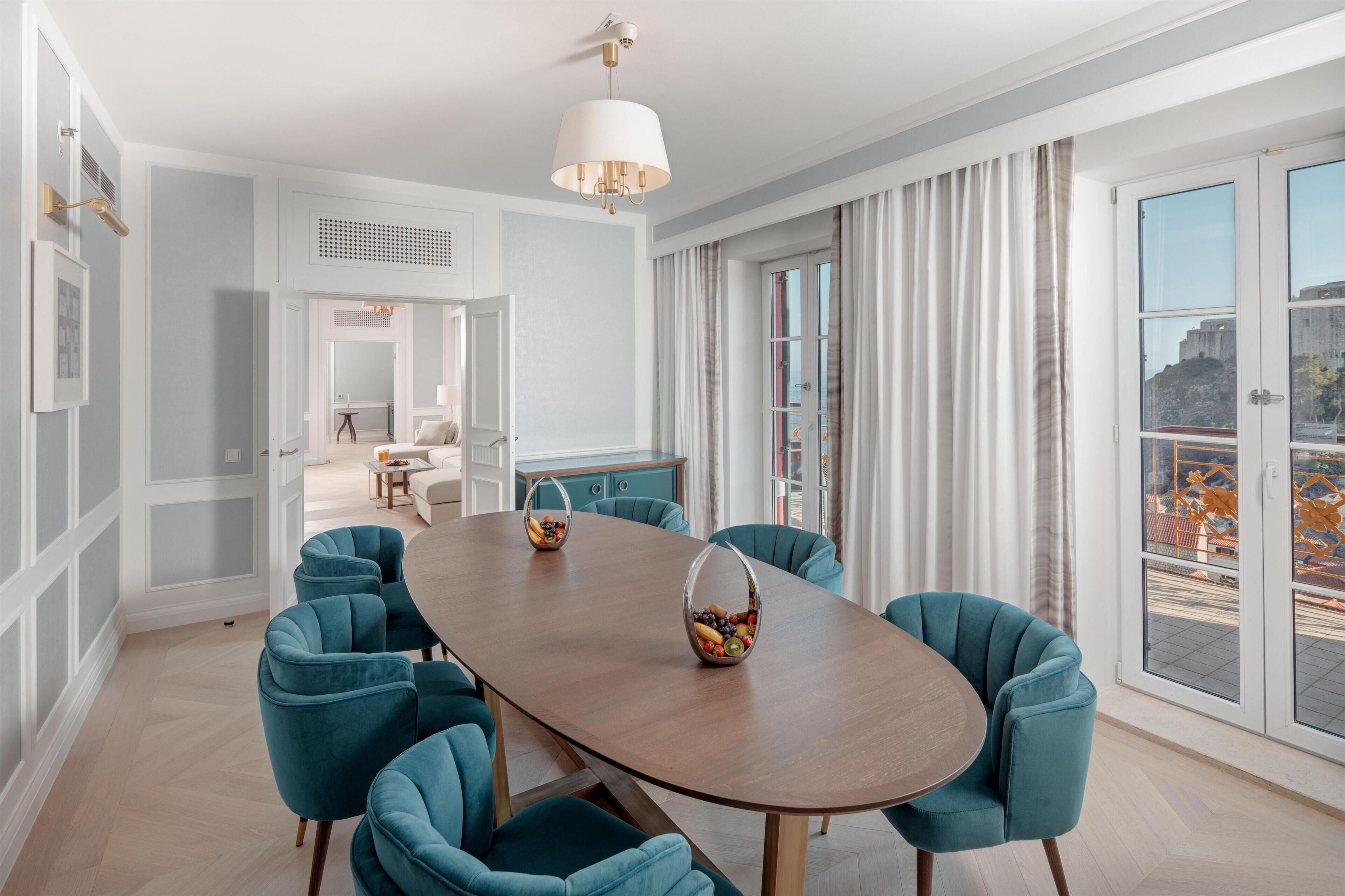A dining area with a wooden table, teal chairs, and a fruit basket.