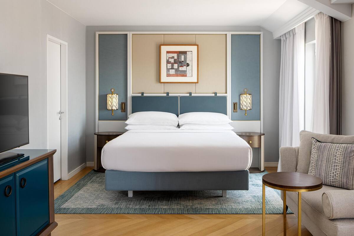 Een hotelkamer met een bed, nachtkastjes, een televisie, een bank en een ingelijst kunstwerk aan de muur.