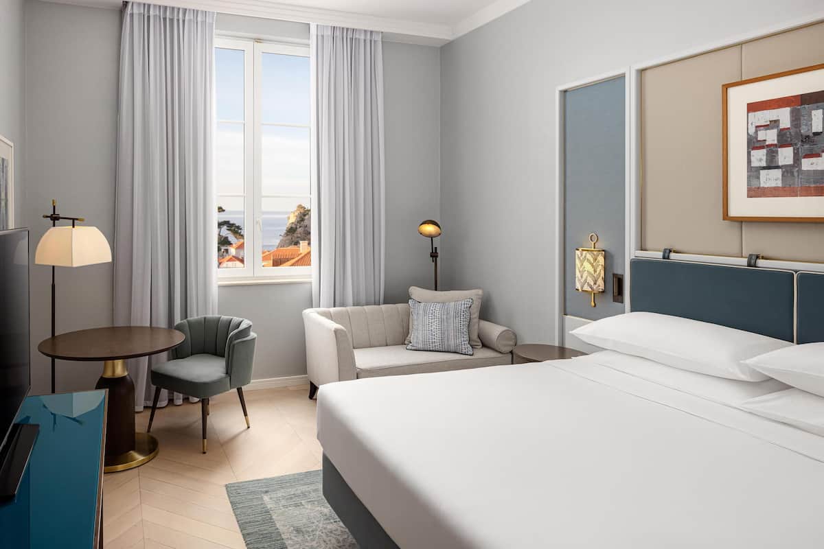 A hotel room with a bed, a sofa, a chair, a desk, a lamp, and a window with curtains.