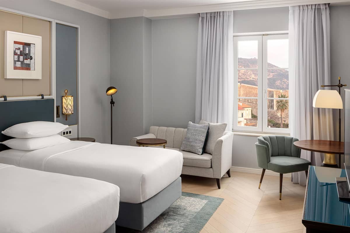 Een hotelkamer met twee bedden, een bank, een stoel, een lamp en uitzicht op de bergen.