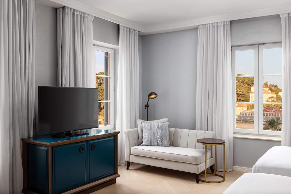Een hotelkamer met een flatscreen televisie, een bank, een klein rond tafeltje en een raam met gordijnen.