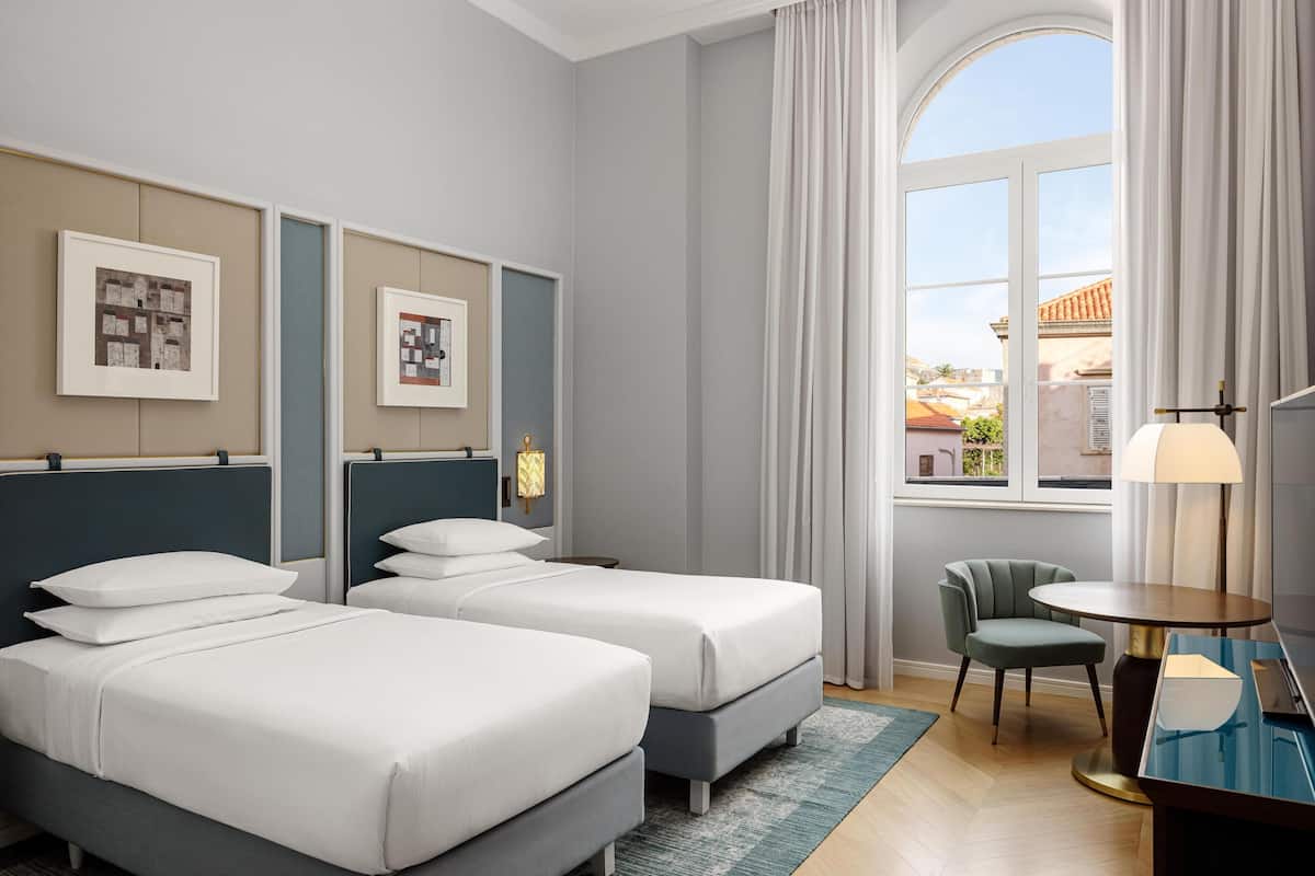 Een hotelkamer met twee bedden, een bureau, een stoel en een raam met gordijnen.