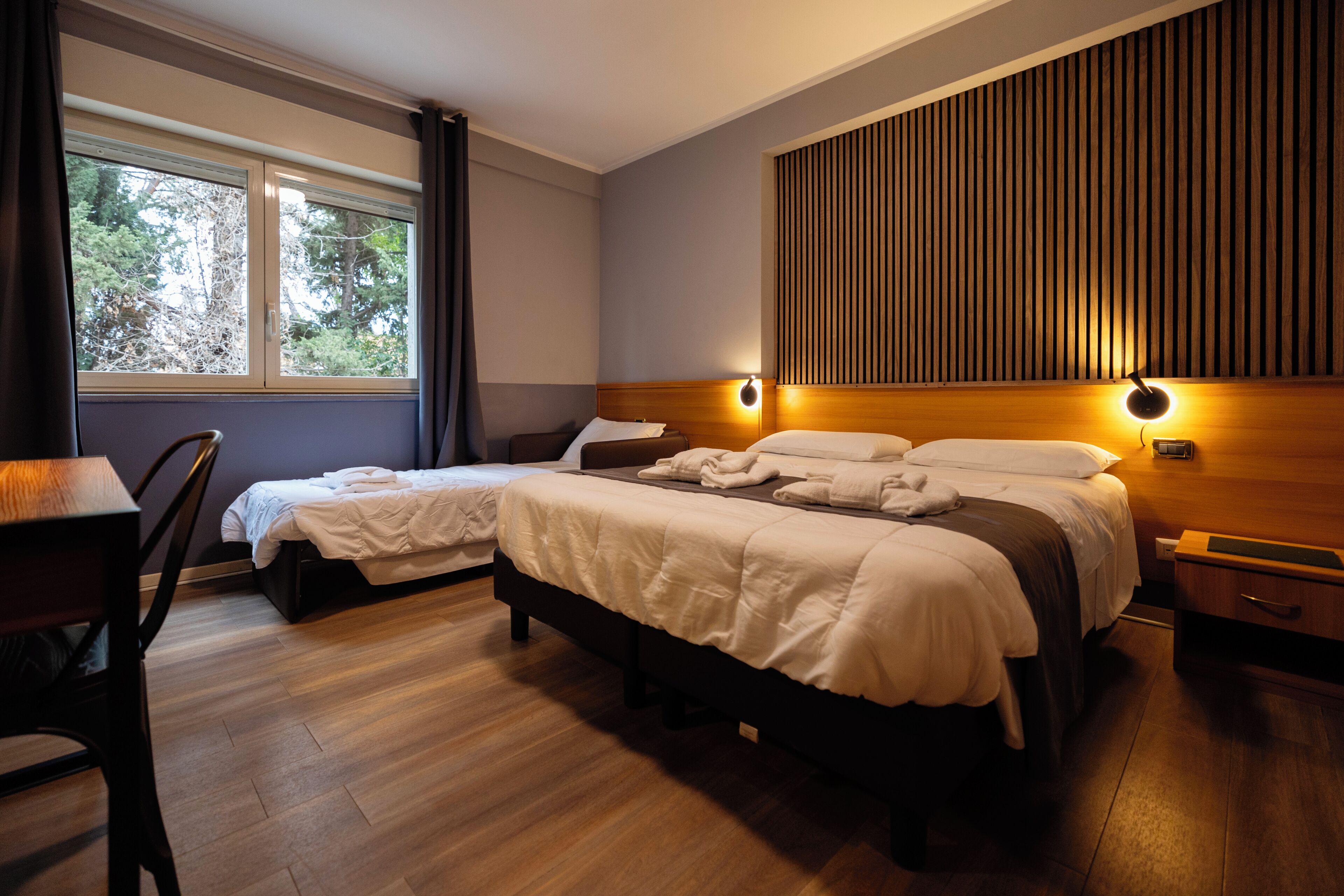 Une chambre d’hôtel avec deux lits, un bureau et une fenêtre avec des rideaux.