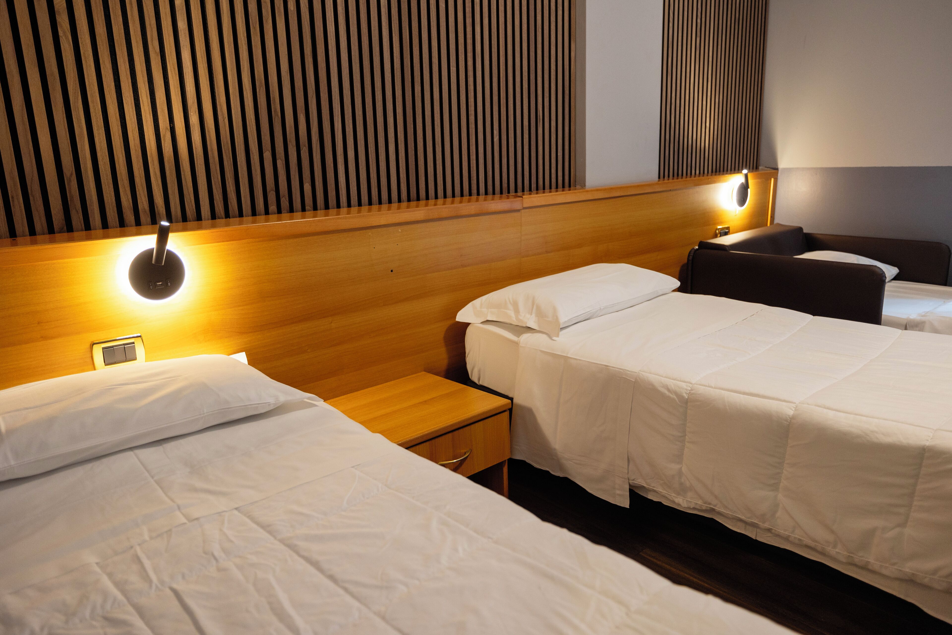 Quarto de hotel com duas camas, cabeceira de madeira, abajures e mesa de cabeceira.