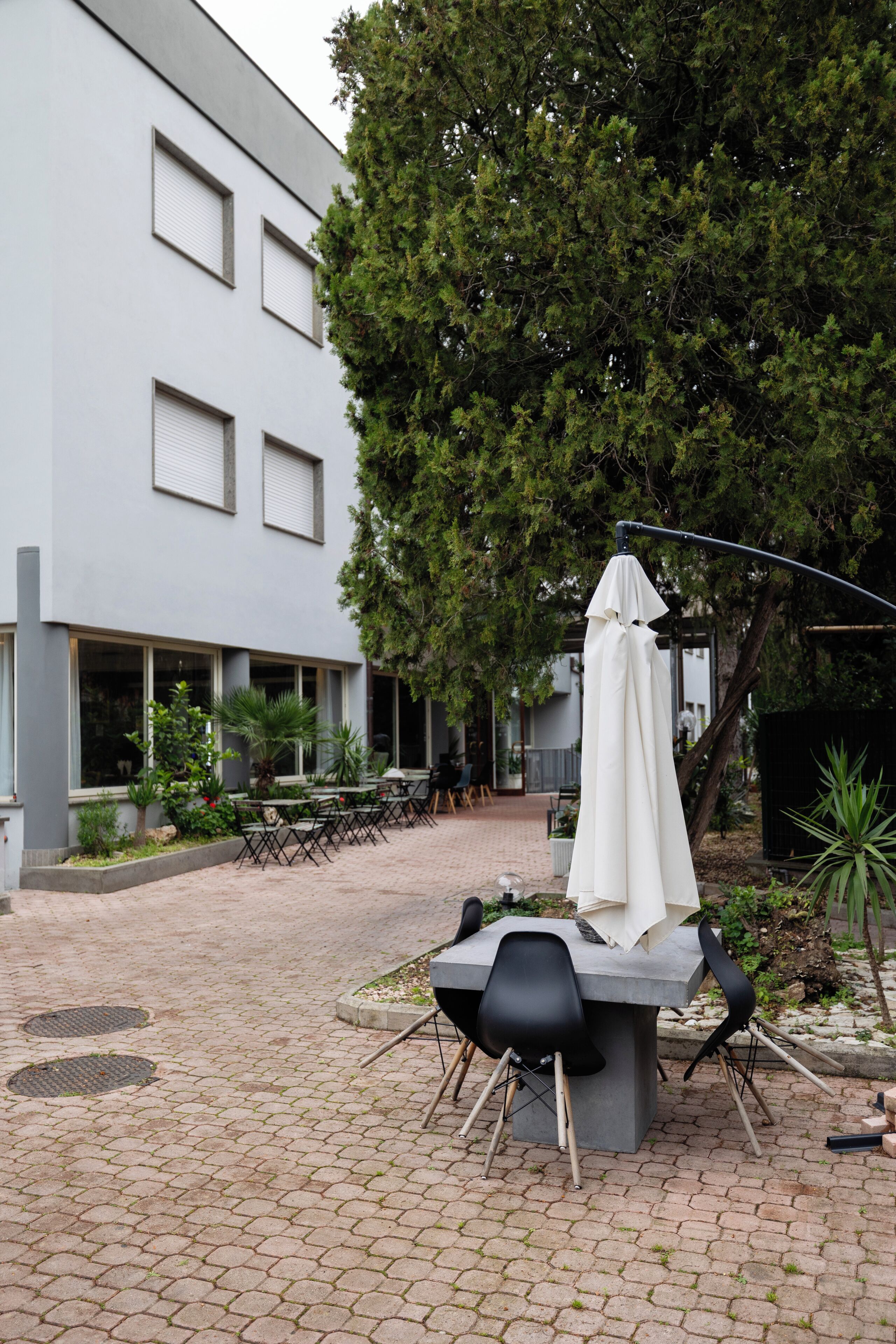 Un espace extérieur aménagé en terrasse avec des tables et des chaises, un coin salon abrité et un bâtiment doté de grandes fenêtres, avec un arbre en arrière-plan.